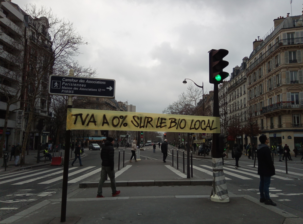 banderole jaune réclamant la TVA à 0% sur le bio local entre 2 feux de circulation