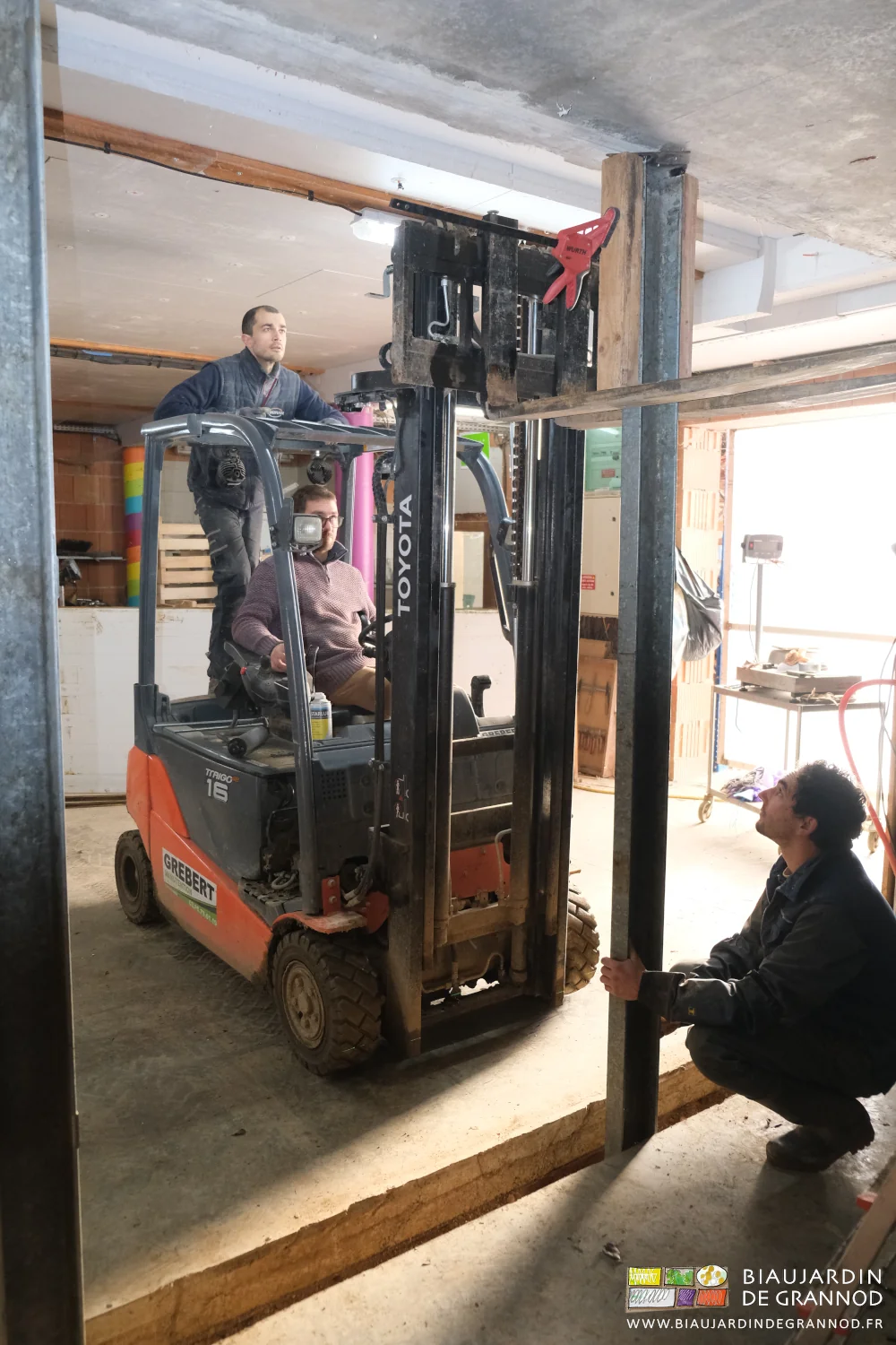 photo d'ensemble, l'un ajustant le pied, l'autre manipulant les fourche du chariot, le dernier guidant le haut