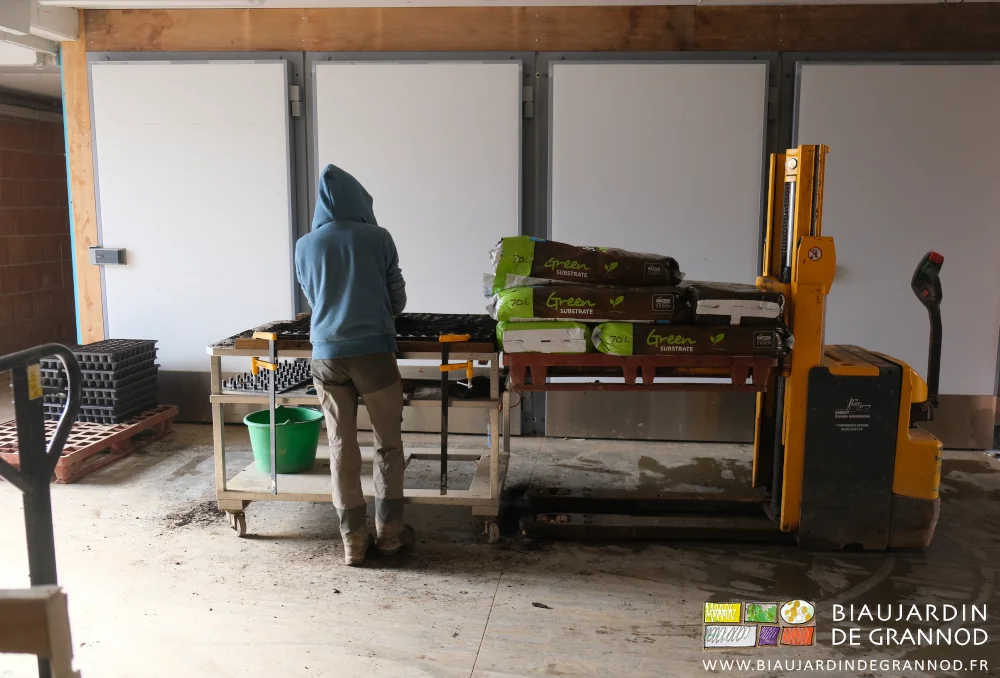 photo d'ensemble du remplissage des plaques de mottes en terreau facilité par une table roulante et des matériels portant les charges