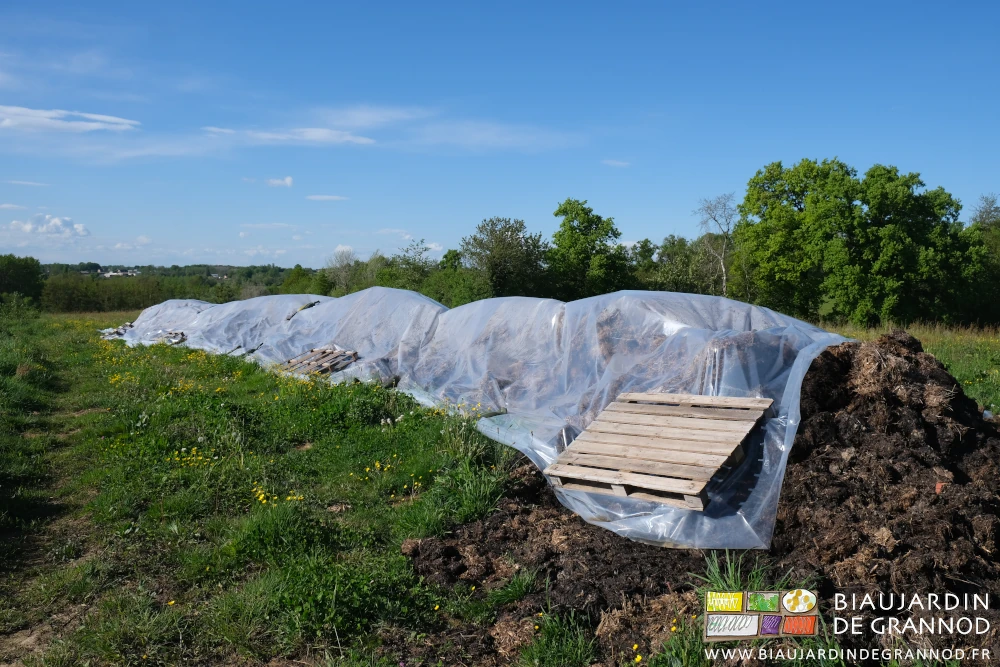 photo du tas de fumier couvert d'une bâche de tunnel lestée de sacs de sable et palettes