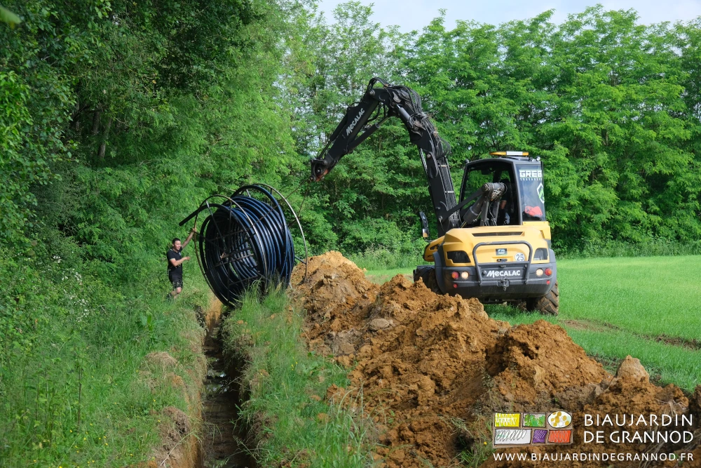 photo de la pelleteuse soutenant un touret de tube en cours de déroulage en fond de tranchée