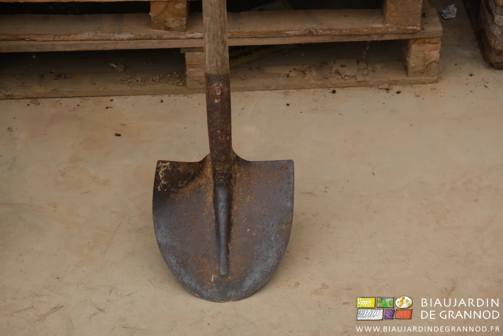 photo d'une pelle ronde avec son manche bois appuyée contre une pile de palettes