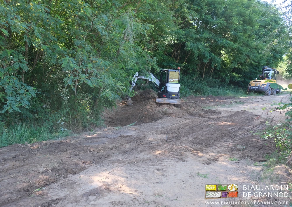 photo de la mini-pelle profilant la terre en dessous du talus du bois de chêne et acacia