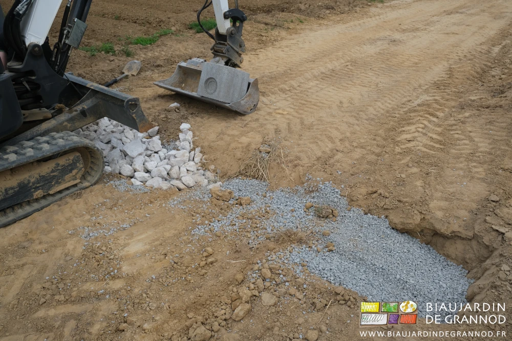 photo dé"taillant la pode à la mini-pelle de gros cailloux par dessus la gravelette de tranchée
