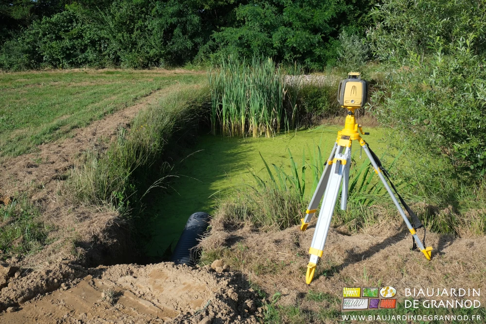 photo du bassin de rétention, tuyau d'évacuation posé et niveau laser installé sur son trépied
